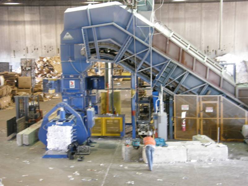 A large blue machine in a warehouse filled with cardboard.