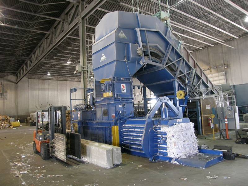 A large blue machine in a warehouse filled with cardboard.