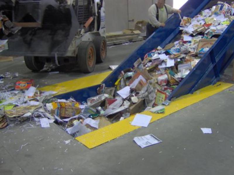 A conveyor belt filled with trash next to a truck.