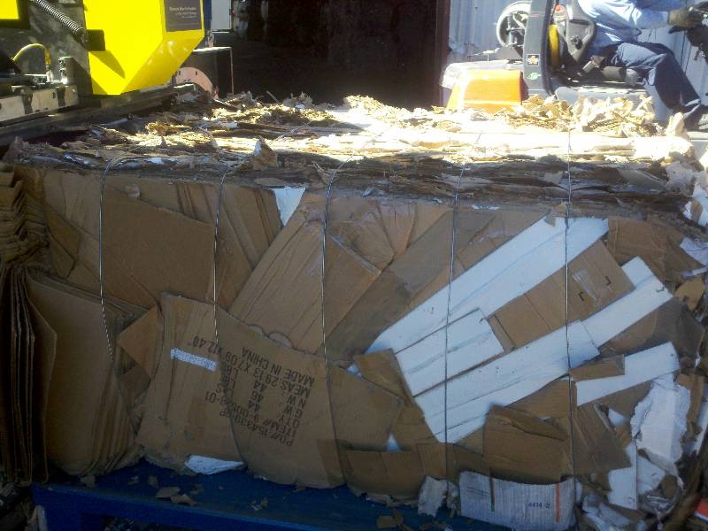 A yellow truck parked next to a pile of cardboard.