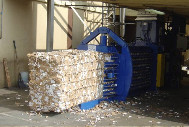 A large blue machine is loading cardboard into the warehouse.