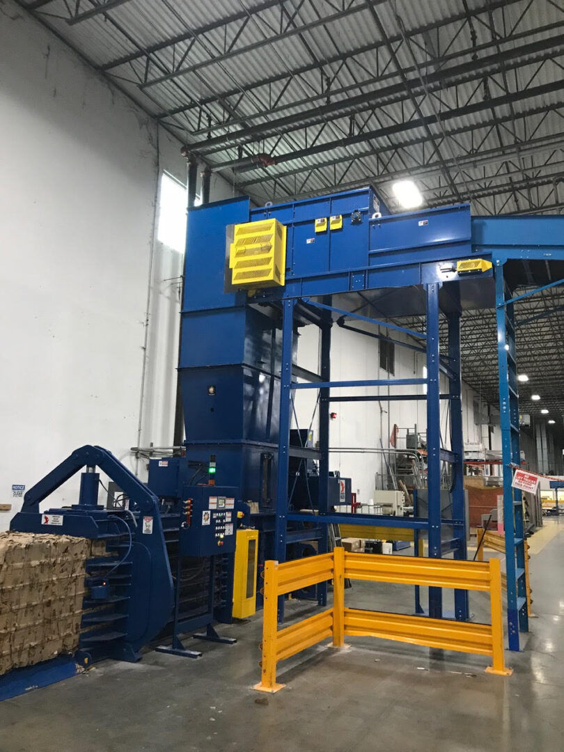 A large blue machine in a warehouse with yellow gate.