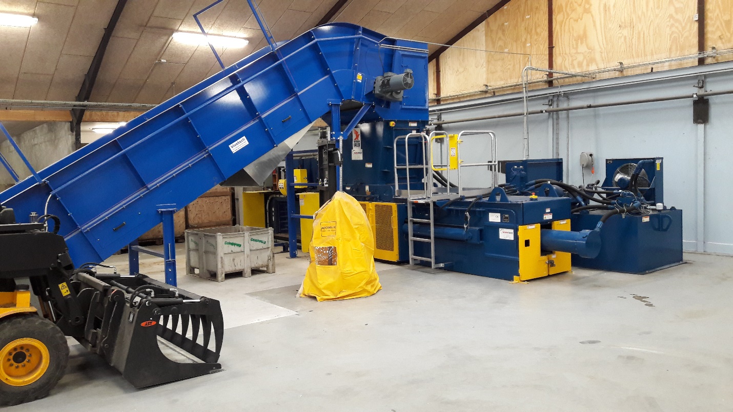 A large blue machine in a warehouse with yellow equipment.