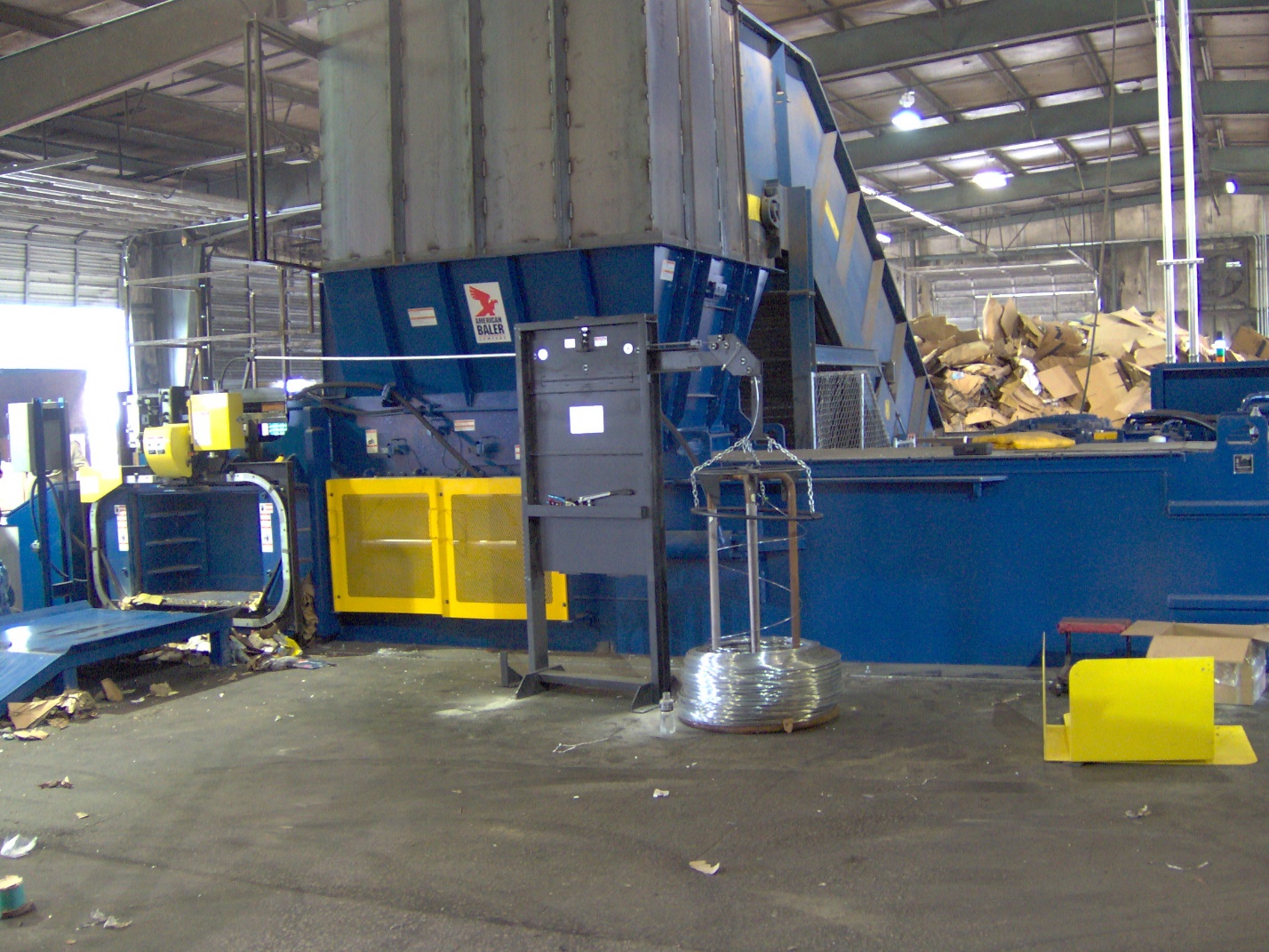 A large blue machine in a warehouse filled with trash.