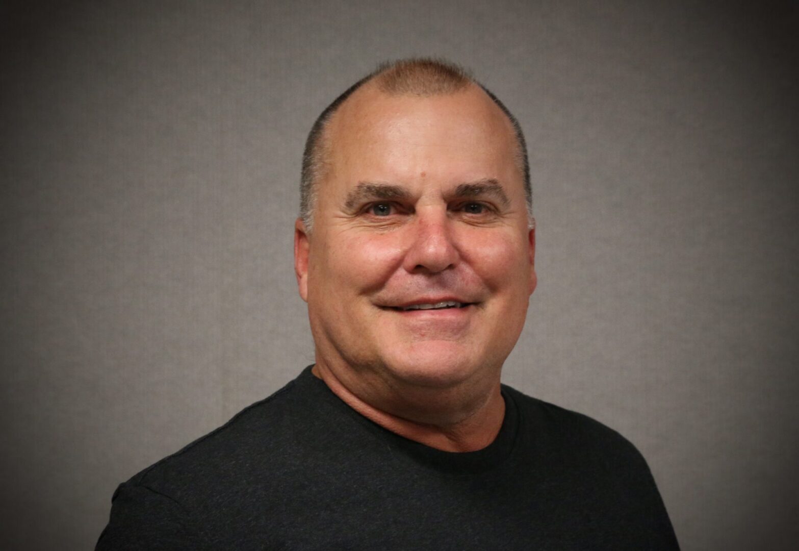 A man with a shaved head and mustache wearing a black shirt.